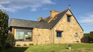 Une maison en pierre avec une grande fenêtre et une plus petite fenêtre agrémentée de volets bleus.