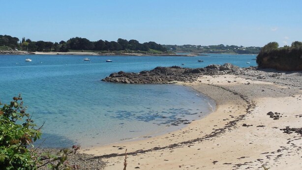 Una spiaggia con acque cristalline, imbarcazioni e affioramenti rocciosi.