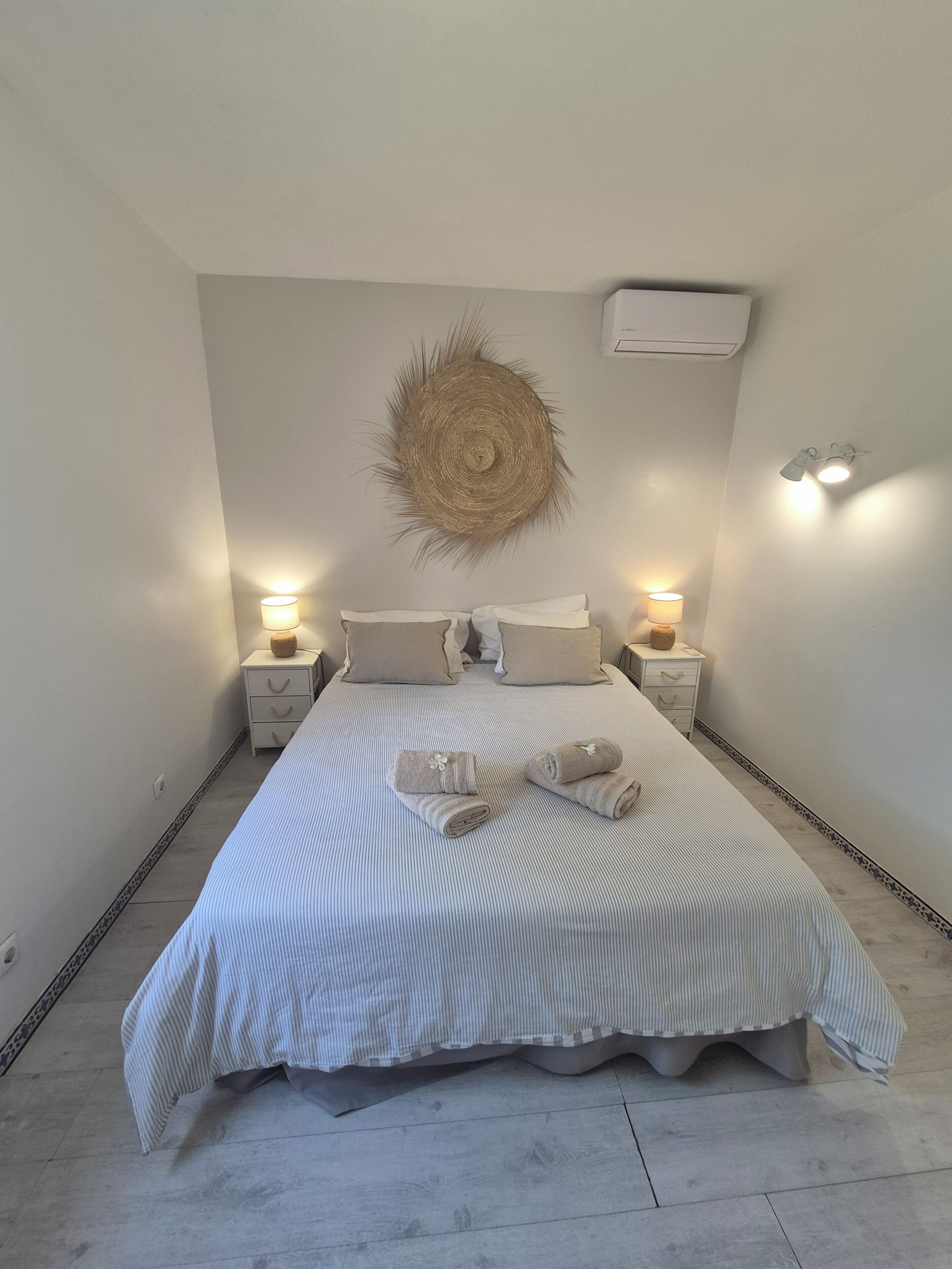 A neatly made bed with striped bedding, two bedside tables with lamps, and a wall-mounted decorative item.