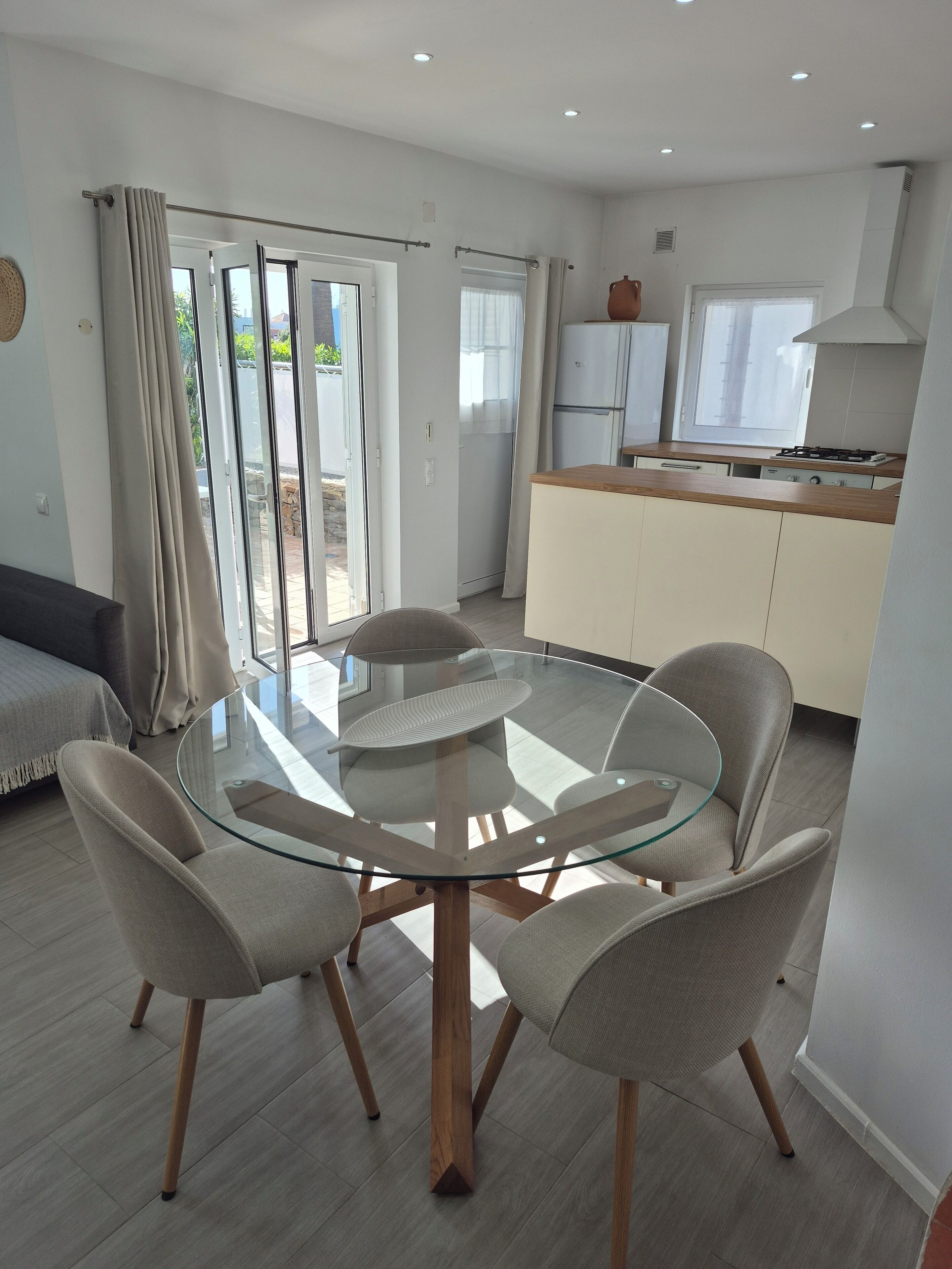 Una cocina moderna con estufa a gas, una zona de comedor con mesa y sillas de vidrio, y un ventanal corredero que da a un espacio exterior.