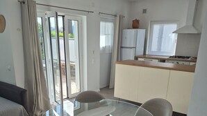 Cuina moderna amb fogó de gas, zona de menjador amb taula de vidre i cadires, i porta corredissa de vidre que dona a una zona exterior.