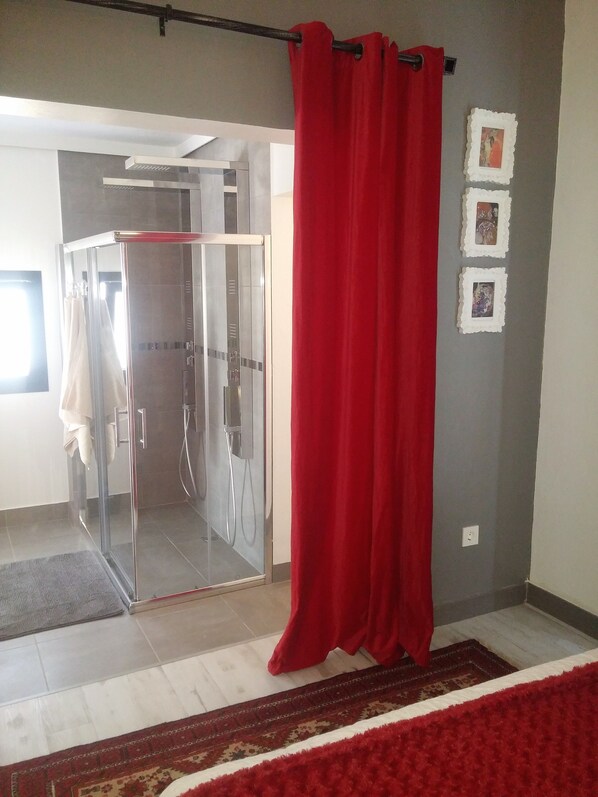 A bathroom with a glass shower enclosure, a red curtain, and a tiled floor.