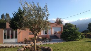 A modern house with a garage, a small patio with outdoor furniture, and a well-maintained garden with a tree and rocks. - PROMOTION! A charming villa with a beautiful garden and a view of the mountains (Calenzana)