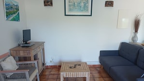 A living room with a blue sofa, a wooden coffee table, a TV on a wooden stand, and a painting on the wall. - PROMOTION! A charming villa with a beautiful garden and a view of the mountains (Calenzana)