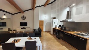 A modern kitchen with a built-in oven, microwave, and sink. There is a dining area with a table and chairs, and a living room with a sofa and a TV.