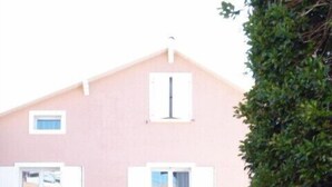 Un bâtiment rose doté de nombreuses fenêtres et d’une porte, entouré de verdure.