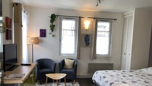 Une chambre moderne avec un lit, deux fauteuils, un bureau avec une télévision et une fenêtre avec des rideaux.