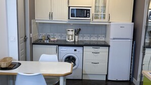 Une cuisine compacte équipée d’un four à micro-ondes, d’un lave-linge et d’un petit coin repas avec une table et des chaises.