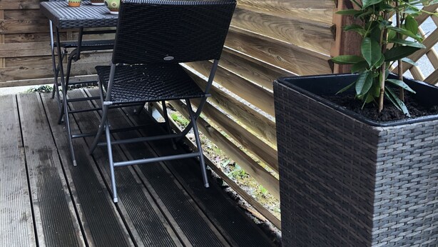 Une terrasse en bois avec une table et des chaises, un pot de fleurs et une structure en treillis.