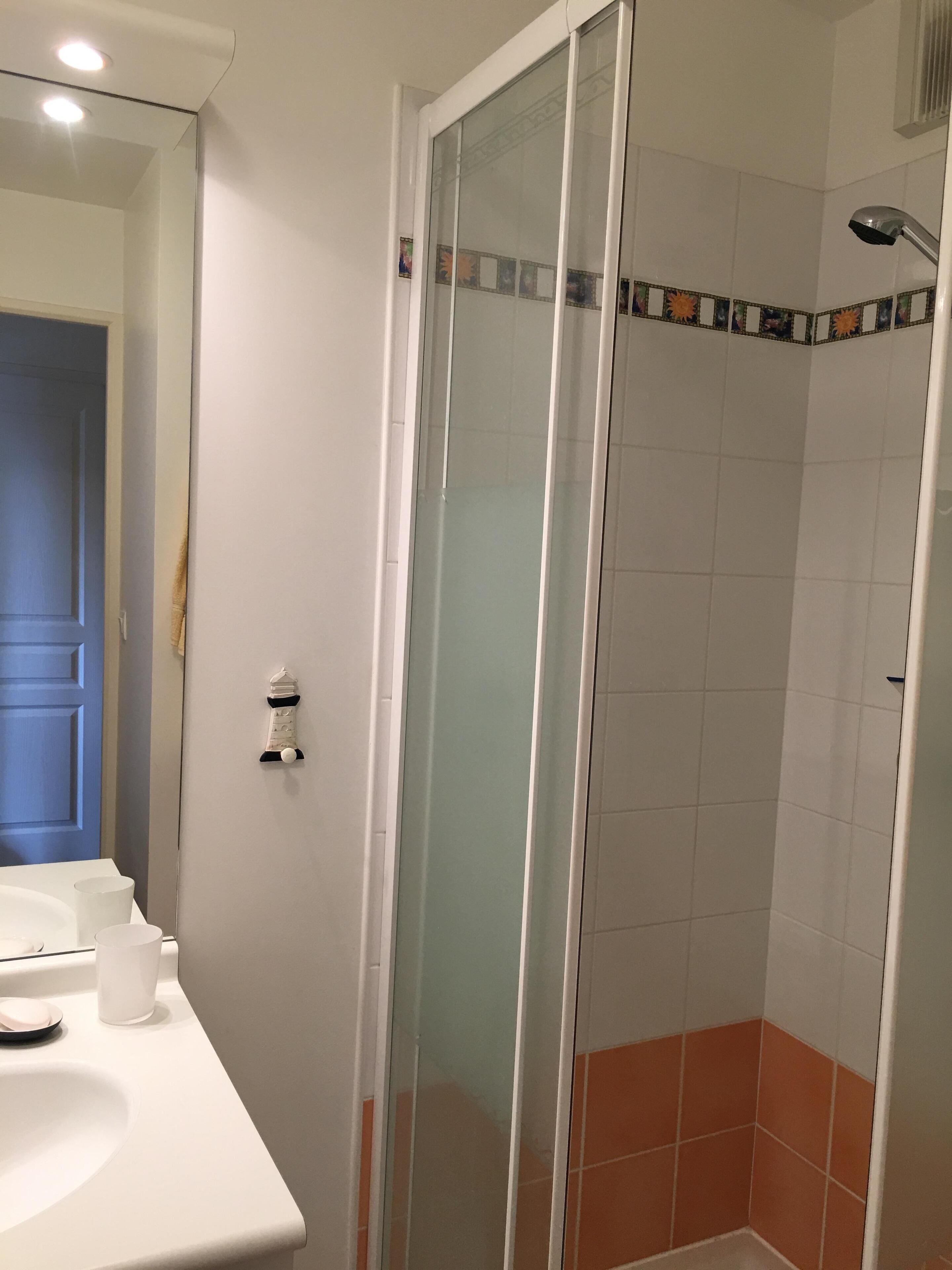 Een badkamer met een douche met glazen wand, een wit wastafelmeubel en oranje tegels in de douche.