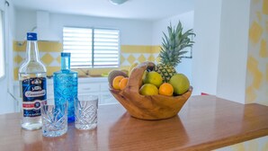 A kitchen with a wooden countertop, a bottle of rum, a glass, and a bowl of fruit.