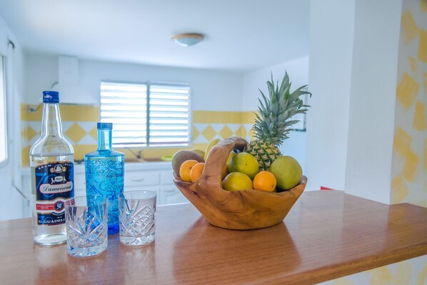 A kitchen with a wooden countertop, a bottle of rum, a glass, and a bowl of fruit. - VILLA LODGE WITH ROOFTOP JACUZZI (sainte-anne)