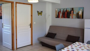 A room with a sofa, a table with a patterned tablecloth, a painting on the wall, and a butterfly decoration. - Single-storey furnished gite in the heart of the village (Bellefontaine)