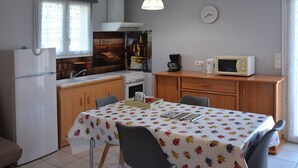 A compact kitchen with a refrigerator, stove, microwave, and a dining table with chairs. - Single-storey furnished gite in the heart of the village (Bellefontaine)