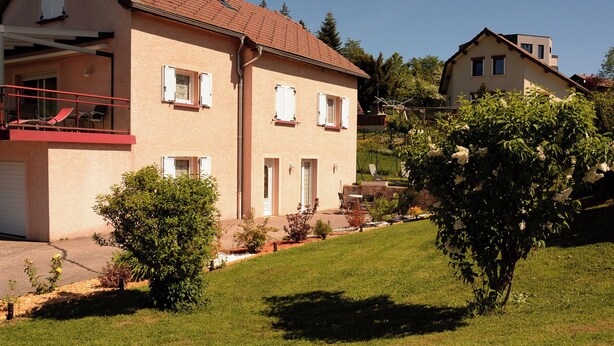 A two-story house with a balcony, a garden with various plants, and a clear sky. - Single-storey furnished gite in the heart of the village (Bellefontaine)