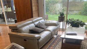 Un salon moderne avec un canapé en cuir, une table basse en verre et une vue sur le jardin grâce à de grandes fenêtres.
