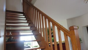 Un escalier en bois avec une rampe, menant à un palier agrémenté d’un banc rembourré de couleur rouge et d’une plante en pot.