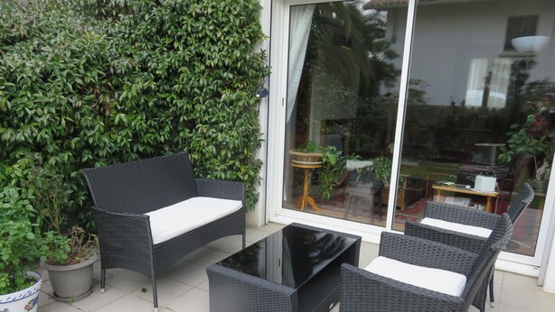 Une terrasse extérieure aménagée avec des meubles en osier, notamment un canapé et deux fauteuils, une petite table et des plantes en pot.