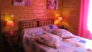 Ein Zimmer mit Holzboden, einem Bett, zwei Nachttischen und zwei Lampen. An den Wänden hängen Blumengemälde.