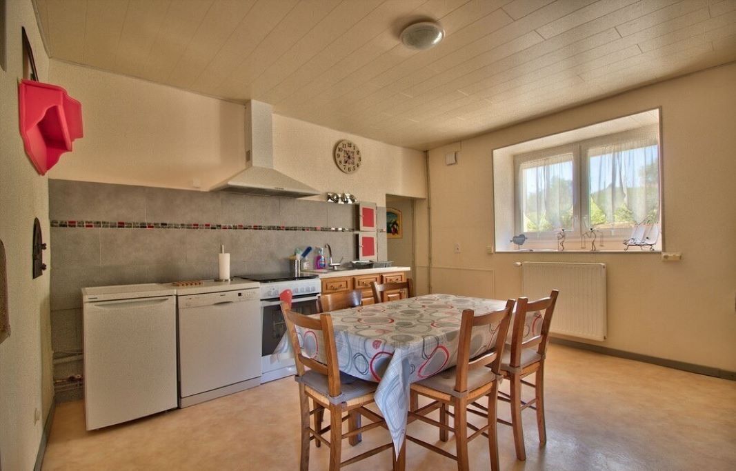 Een compacte keuken met een eettafel en stoelen, een klok aan de muur en een raam met gordijnen.