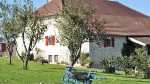 Un bâtiment en pierre avec un toit recouvert de tuiles rouges, un banc au premier plan et une pelouse verdoyante.