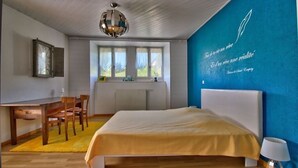 Une chambre à coucher avec un lit, un bureau et une chaise. Il y a une fenêtre qui donne sur un paysage verdoyant.