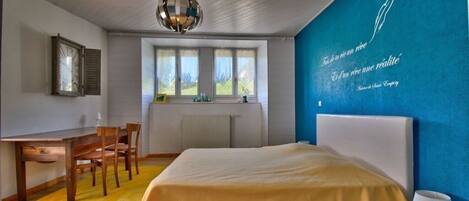 A bedroom with a bed, a desk, and a chair. There is a window with a view of greenery outside.