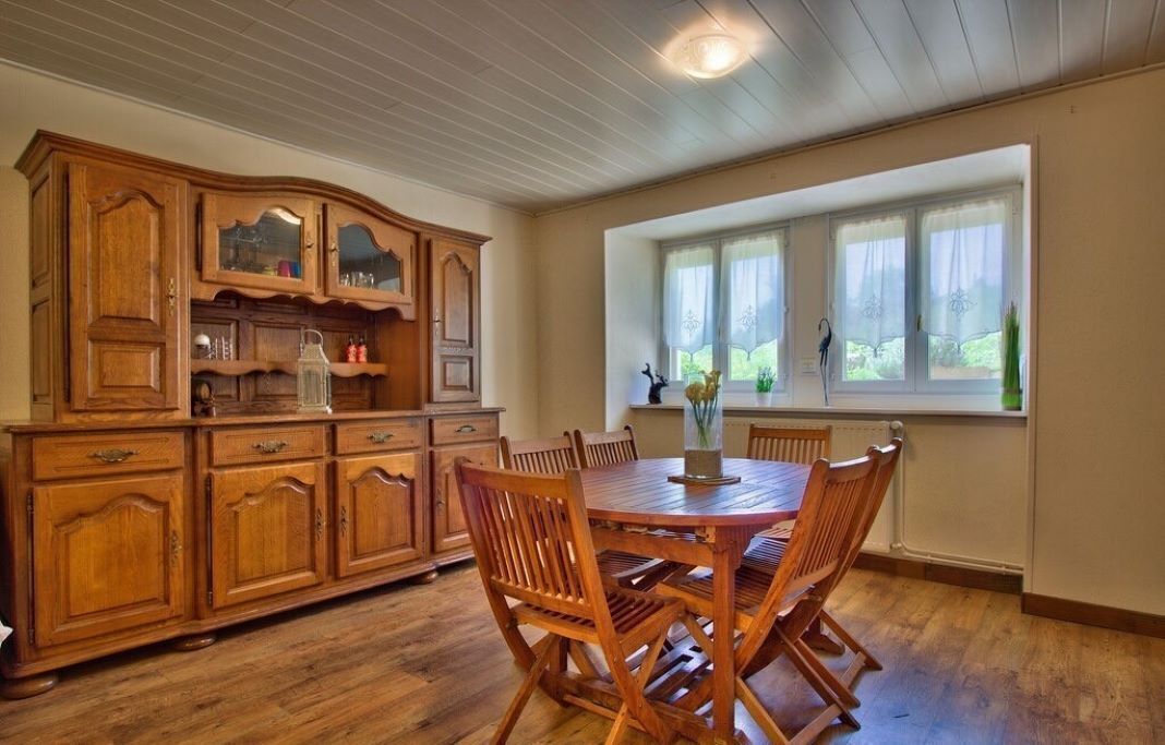 A dining area with a wooden table and chairs, a wooden cabinet with glass doors, and a window with curtains.