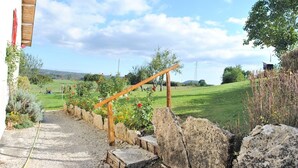 Un sentier de jardin mène à une structure en bois dont un côté est bordé d’un mur de pierres.