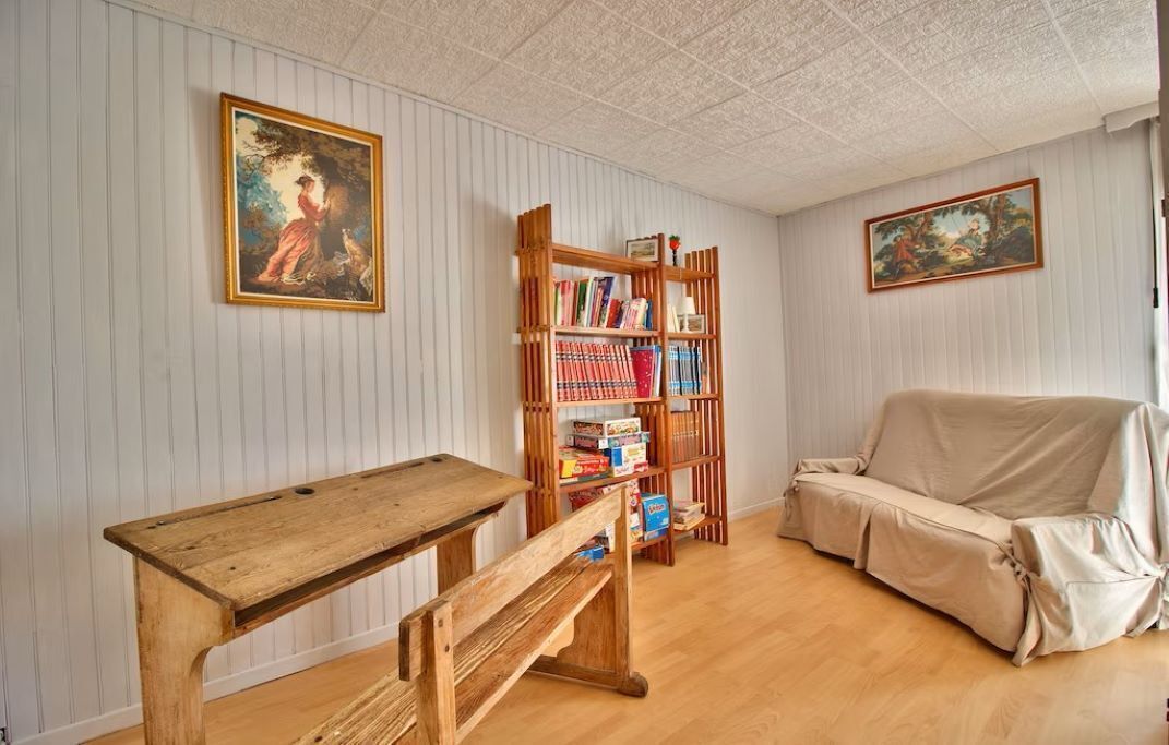 Une pièce avec une table en bois, un canapé recouvert d’un tissu, une bibliothèque et deux tableaux encadrés accrochés aux murs.