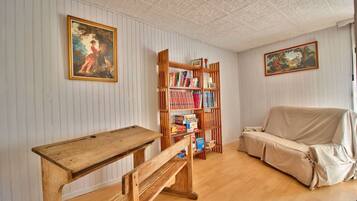 Une pièce avec une table en bois, un canapé recouvert d’un tissu, une bibliothèque et deux tableaux encadrés accrochés aux murs.