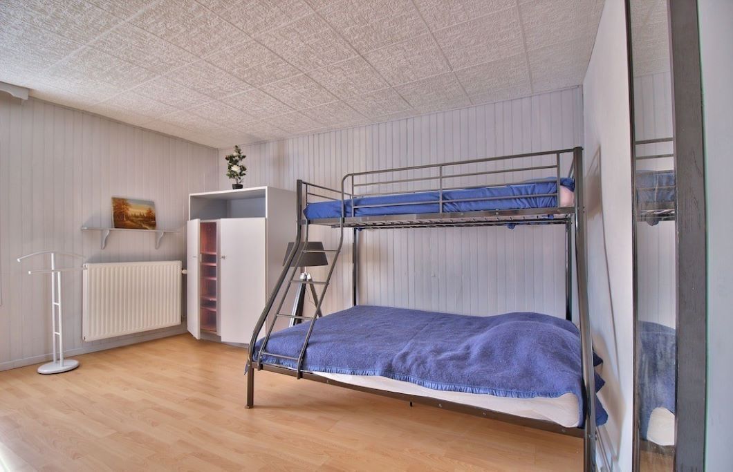 Une chambre avec un lit superposé, un radiateur, une étagère avec un tableau et une échelle.