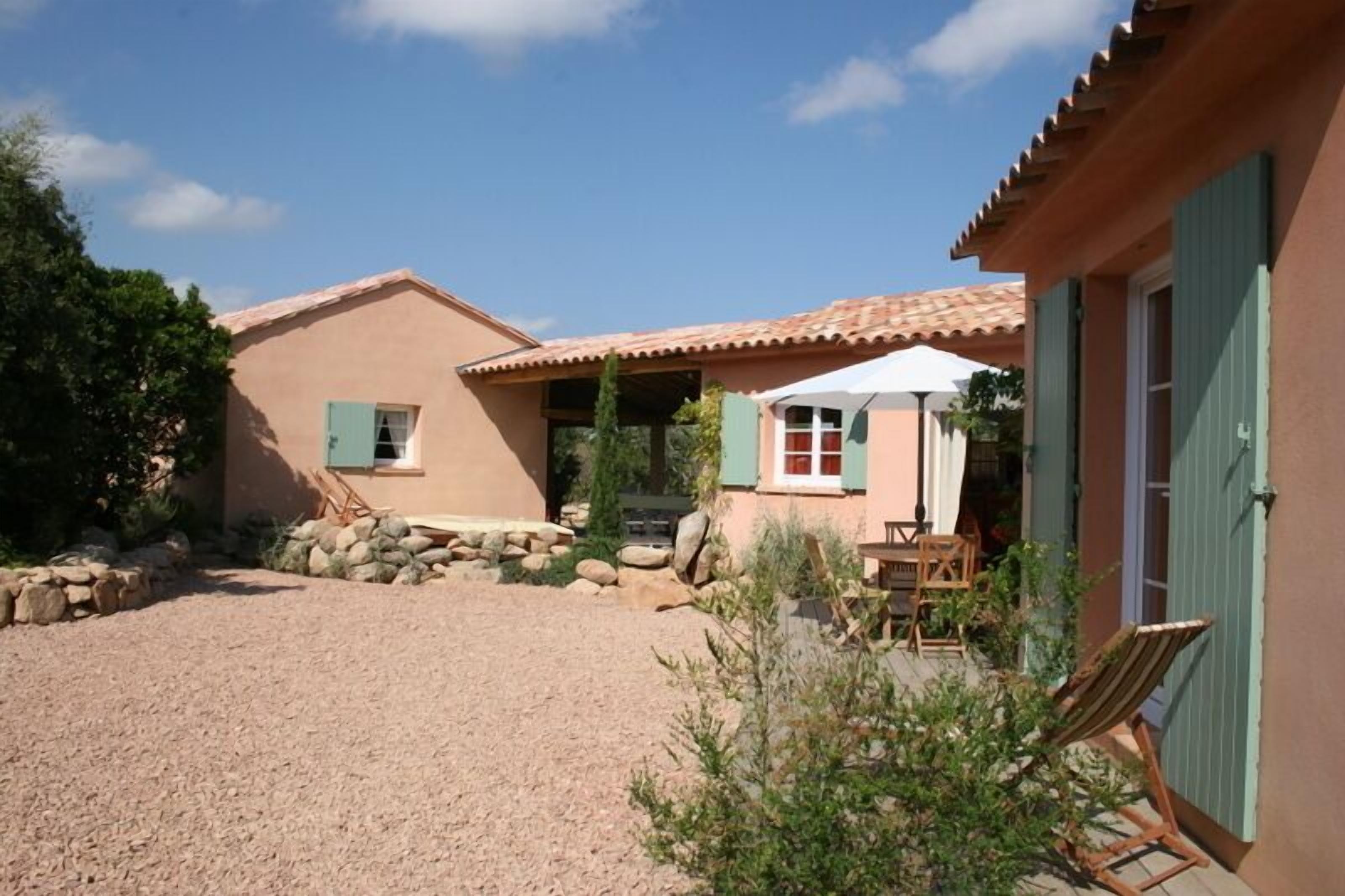 Une maison avec une allée en gravier, une terrasse avec des meubles d’extérieur et un espace couvert avec une table et des chaises.