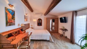 Hotelkamer met een bed, een houten bureau, stoel, lampen, kunst en een televisie, met uitzicht op het omliggende landschap.