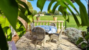Een terras buiten met rieten meubels, een tafel met een blauwe tafelkleed en potplanten.