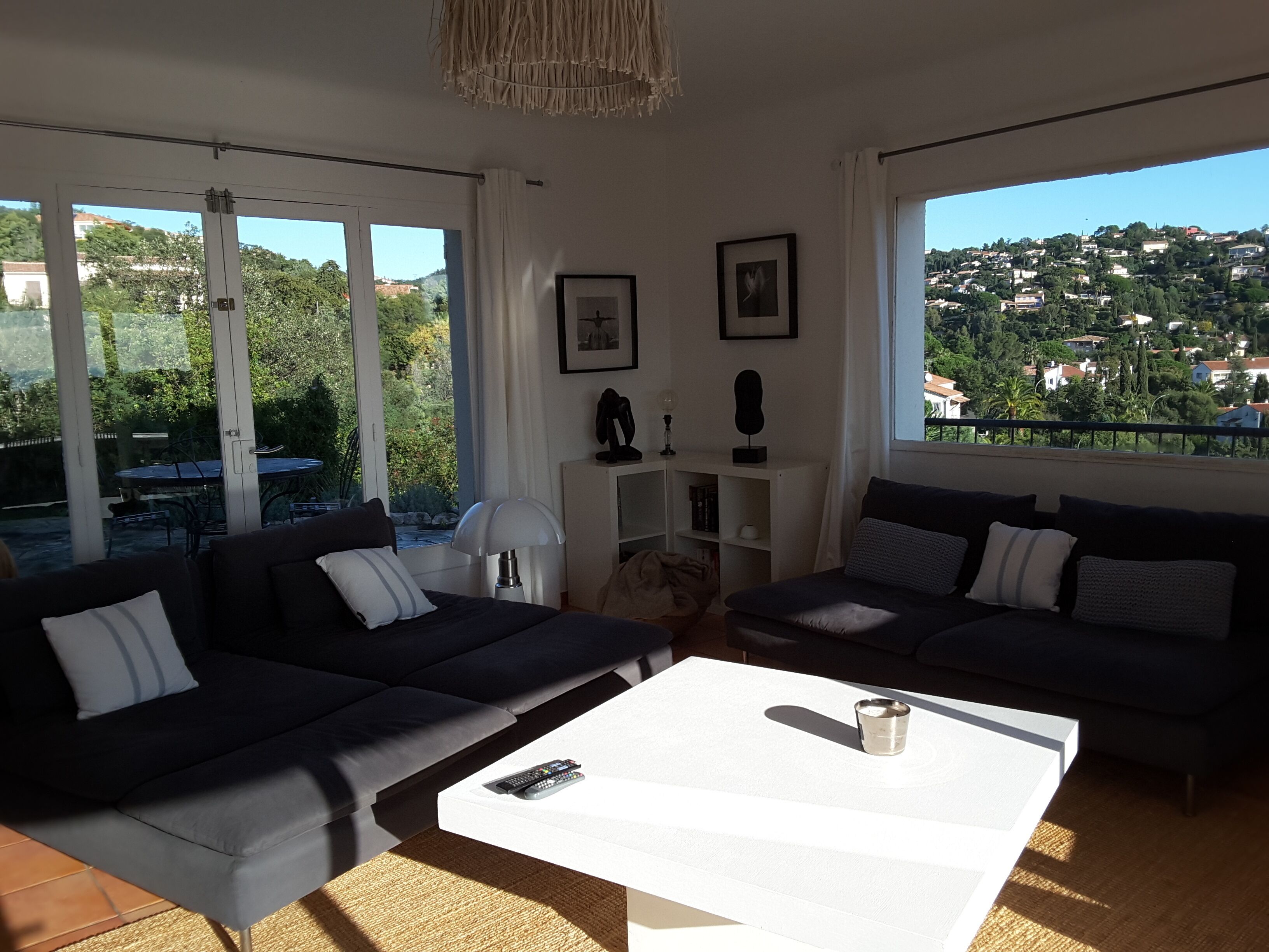 A modern living room with two dark sofas, a white coffee table, and a view of a green landscape through large windows.