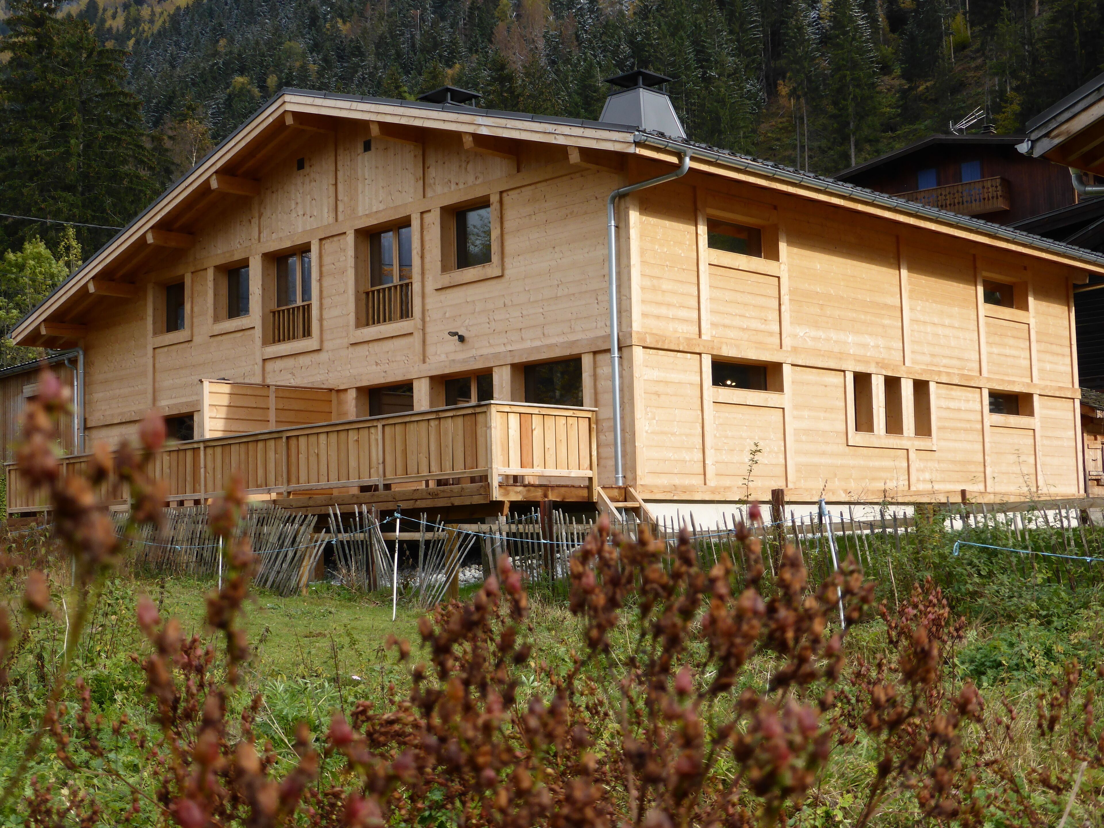 Una baita di legno con diverse finestre e un balcone, immersa in un paesaggio naturale.
