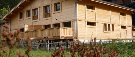 Una baita di legno con diverse finestre e un balcone, immersa in un paesaggio naturale.