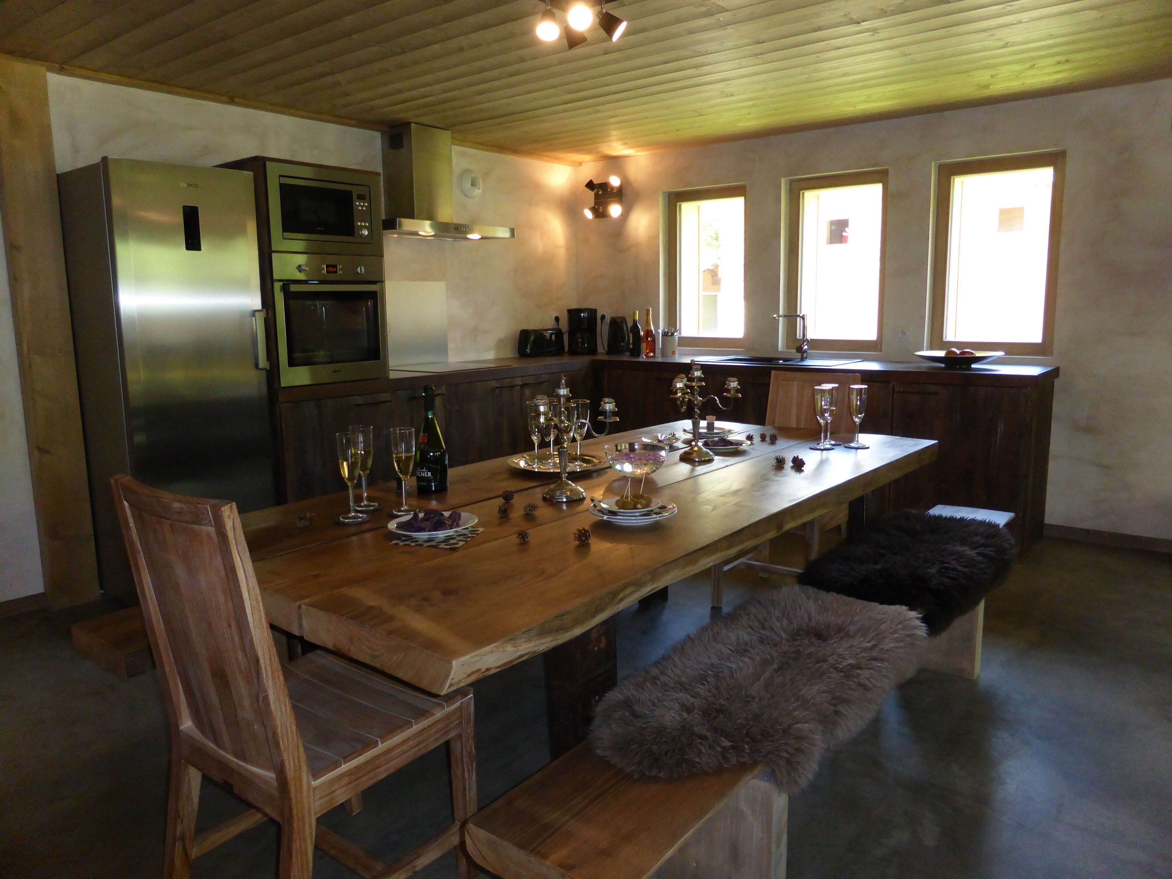 A modern kitchen with a wooden dining table set for a meal, equipped with wine glasses and bottles.
