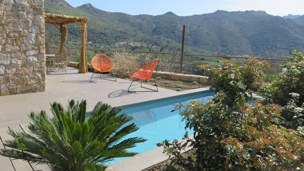 Ein Poolbereich mit Steinmauern, zwei orangefarbenen Liegestühlen und Blick auf Berge.