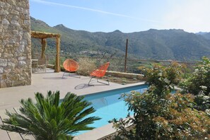 Ein Poolbereich mit Steinmauern, zwei orangefarbenen Liegestühlen und Blick auf Berge.