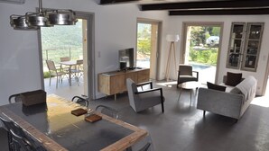 Ein modernes Wohnzimmer mit Essbereich, einer Sofagarnitur, einem Fernseher und Blick auf einen Pool und Berge.