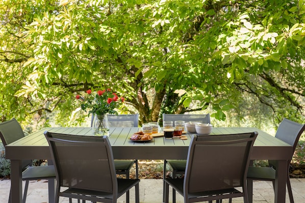 Een eettafel buiten met stoelen, een vaas rode bloemen en een bord eten.