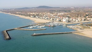 An aerial view of a coastal town with a marina, sandy beach, and residential buildings. - ----------- (Marseillan)