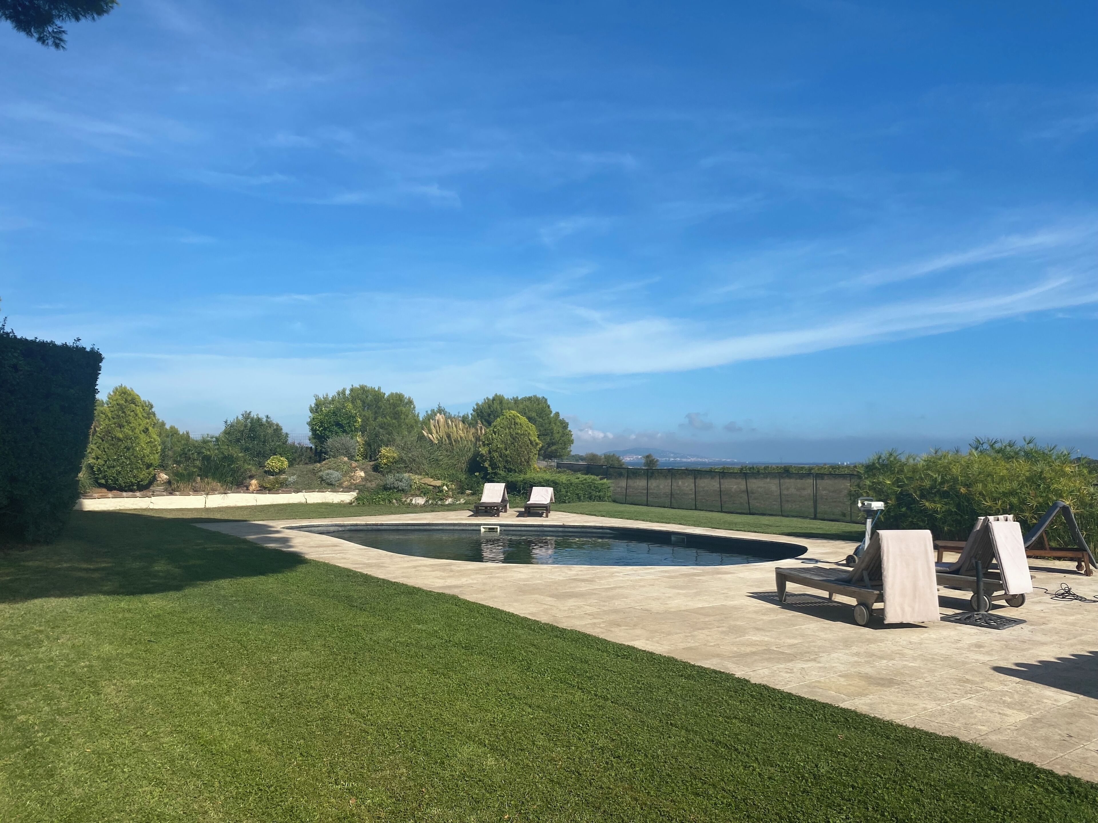 Un patio trasero con piscina, dos sillones de descanso y vista al océano.