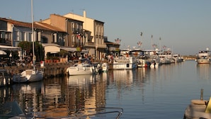 A marina with boats docked along the waterfront, surrounded by buildings with balconies and outdoor seating areas. - ----------- (Marseillan)