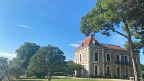 A large, historic building with a red-tiled roof, surrounded by a well-maintained lawn and several trees. - ----------- (Marseillan)