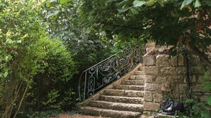 Un escalier en pierre avec des rampes métalliques, entouré d’une végétation luxuriante.