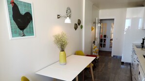 Une cuisine moderne avec une table blanche, des chaises jaunes, un vase contenant des fleurs séchées et une horloge au mur.