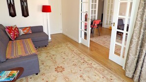 Un salon avec un canapé gris, un tapis à motifs et deux figurines décoratives en bois.
